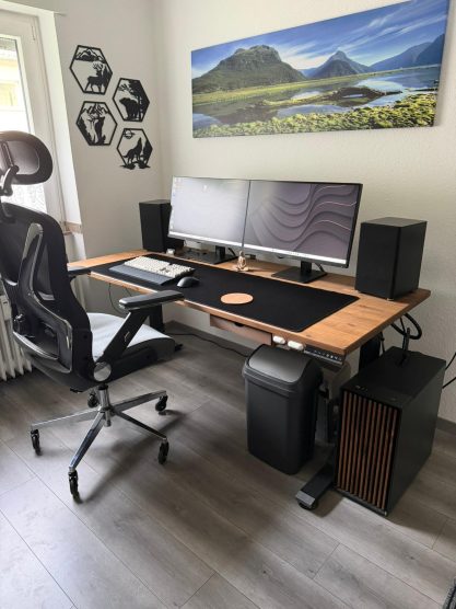 Ein moderner Schreibtisch mit zwei Monitoren, Lautsprechern und einem ergonomischen Stuhl.